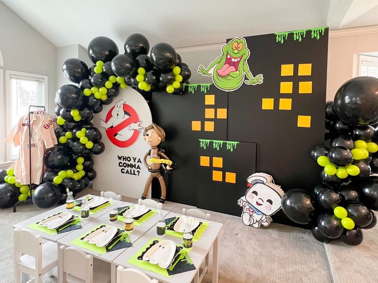 a room decorated for halloween with black and green balloons, white tablecloths and decorations