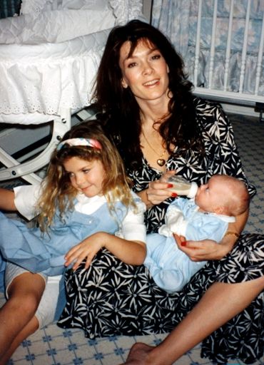 a woman and two children sitting on the floor in front of a baby crib