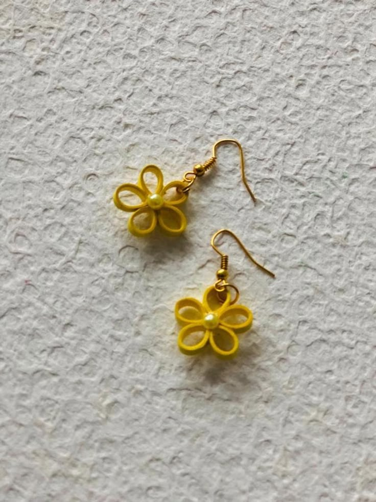 two yellow flower shaped earrings sitting on top of a white surface with gold colored wire