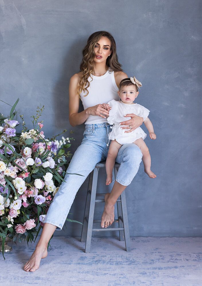 a woman sitting on a stool holding a baby in her arms and flowers behind her