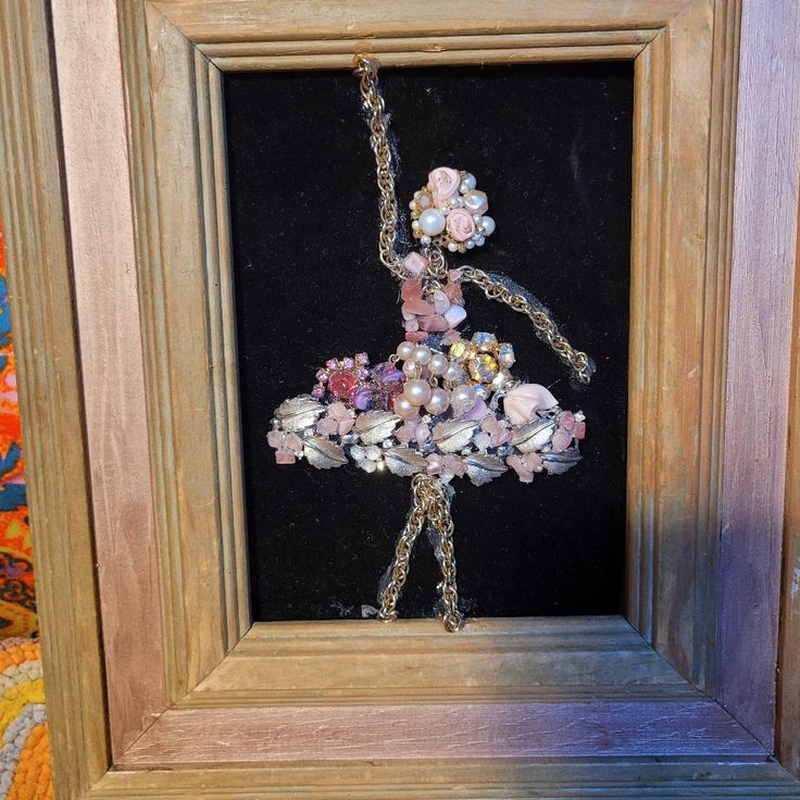 a ballerina in a dress made out of seashells and pearls hangs from a frame