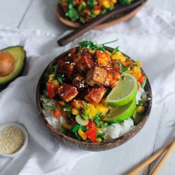 a bowl filled with rice and vegetables next to chopsticks on a white table