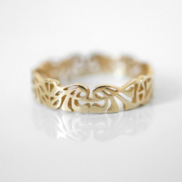 a gold ring with an intricate design on the outside and inside, sitting on a white surface