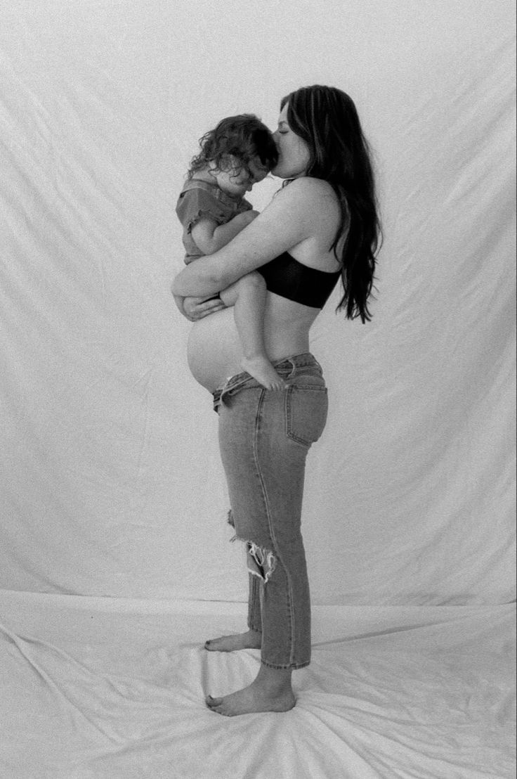 a woman holding a baby in her arms while posing for a black and white photo