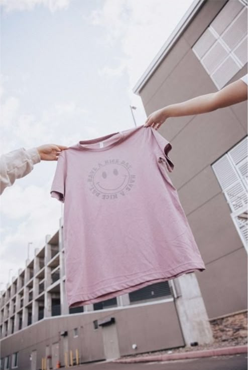 two people holding up a pink t - shirt in front of a large apartment building