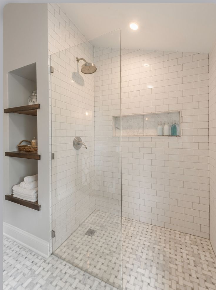 a walk in shower sitting next to a white tiled wall and floor with shelves on each side