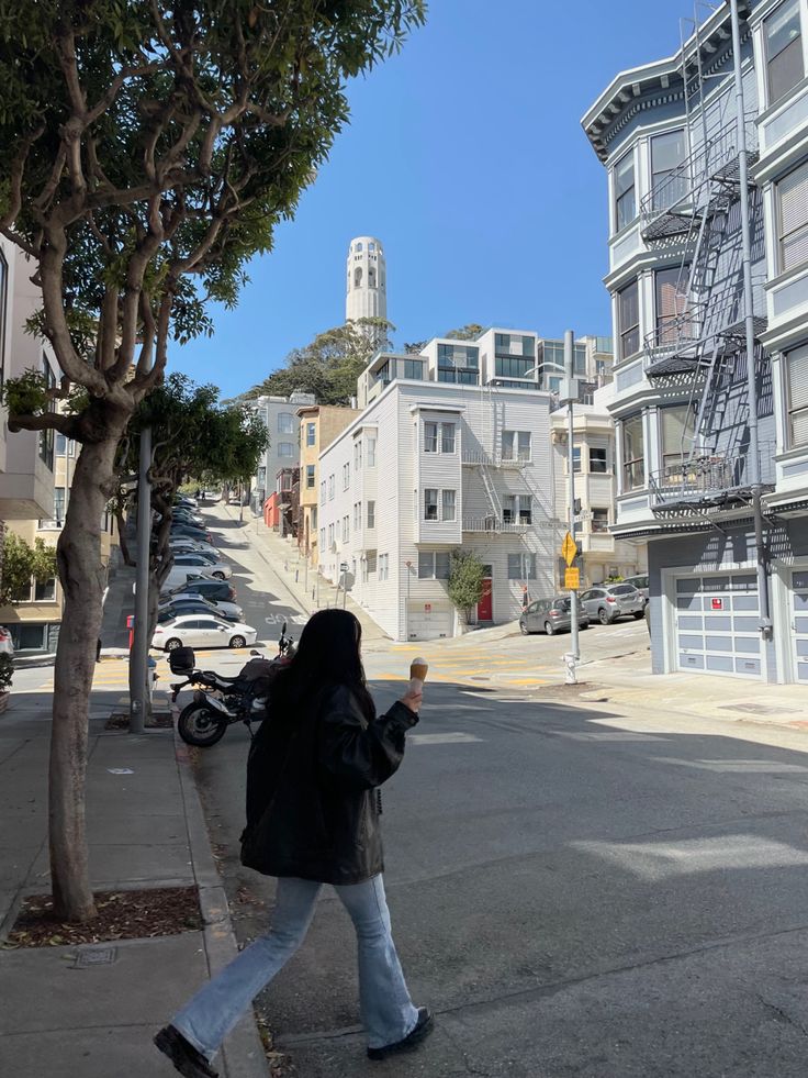 a woman is walking down the street with her cell phone in hand and buildings behind her