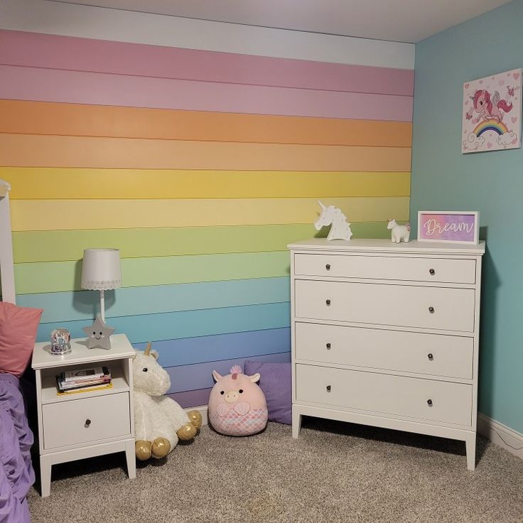 a bedroom with pastel rainbow wallpaper and white dressers in the foreground