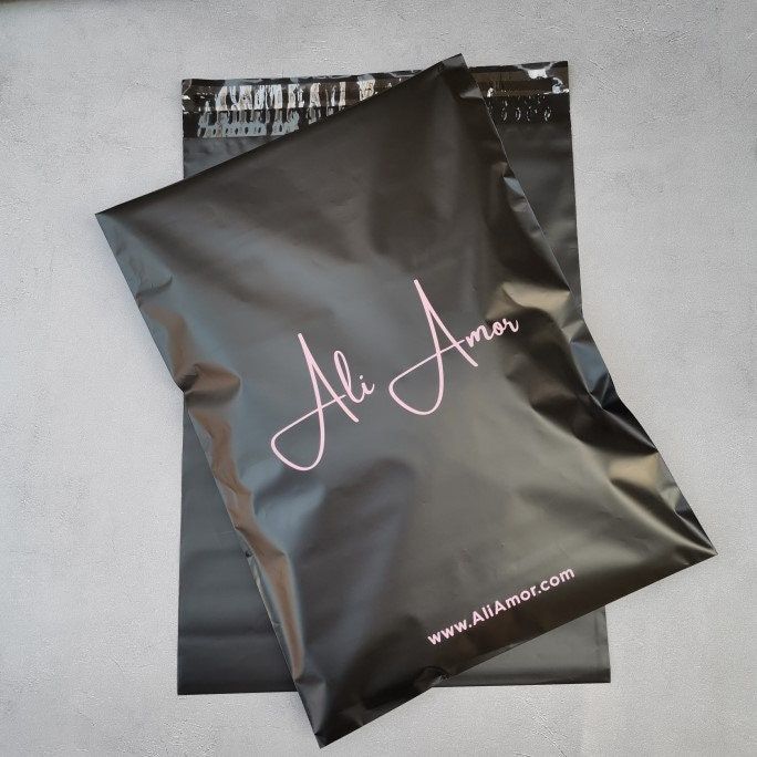 a black paper bag with the name alc amn printed on it, sitting against a white wall