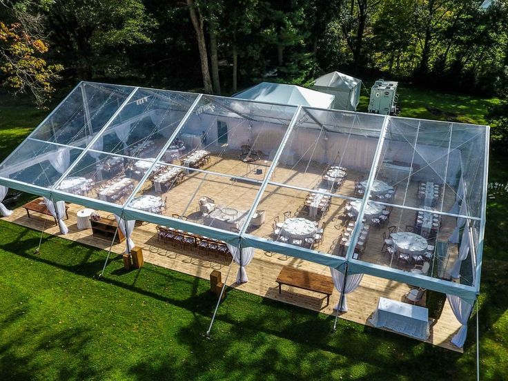 an outdoor dining area with tables and chairs under a clear tent on the grass in front of trees