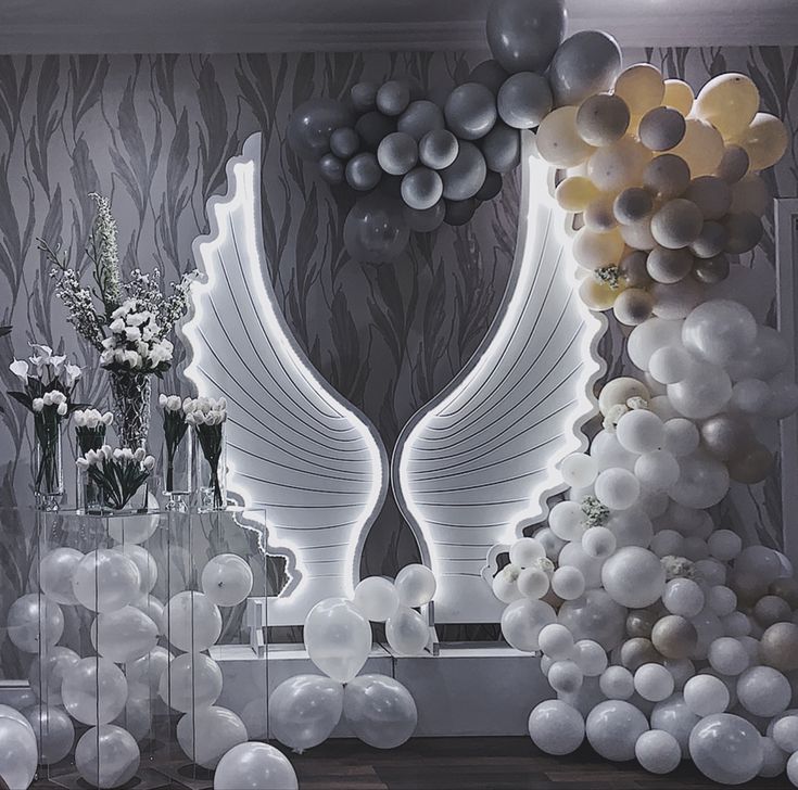 balloons, flowers and vases are arranged in front of a wall with an angel wing