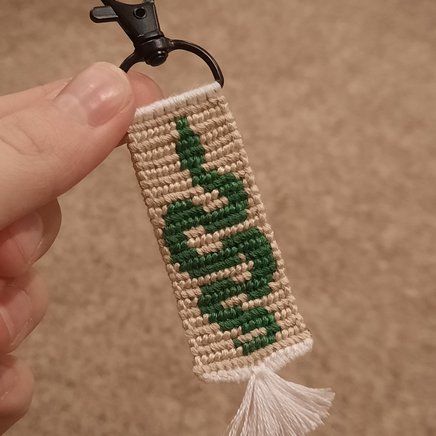 a hand holding a green and white beaded keychain with an arrow on it