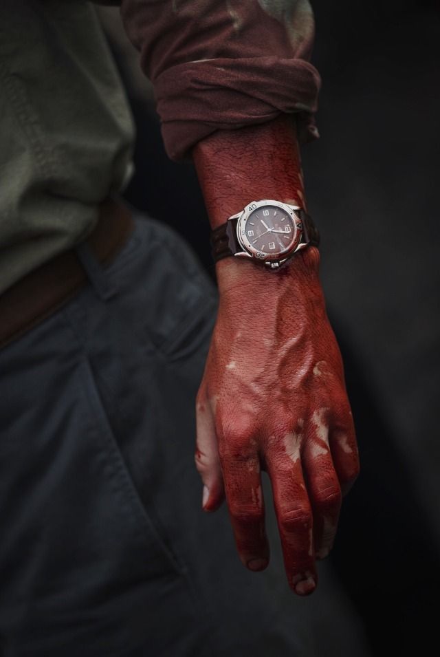 a person's hand with red paint on it and a watch in the other hand