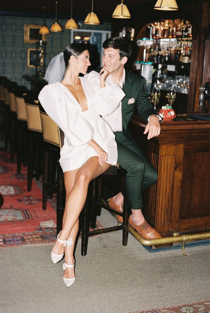 a man and woman sitting at a bar posing for the camera with their legs crossed