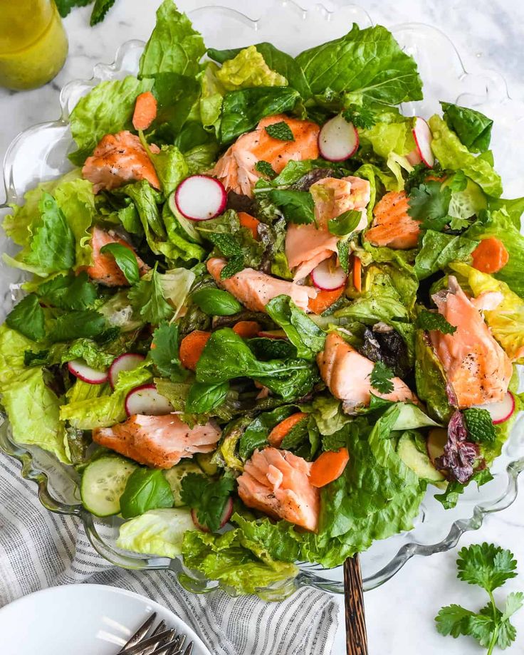 a salad with salmon, lettuce and radishes in it on a glass plate