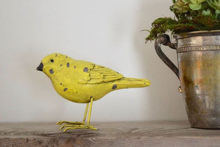 a yellow bird sitting on top of a wooden table next to a potted plant