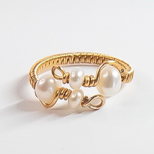 The ring features natural pearls that are carefully wire-wrapped in a unique and intricate design, creating a one-of-a-kind piece. The adjustable band ensures a perfect fit for any finger, making it a versatile addition to any jewelry collection. The combination of natural pearls and handmade wire wrapping makes this ring a truly unique and special piece that will be treasured for years to come. Perfect for any occasion, this pearl ring is an excellent choice for those who appreciate the beauty of natural materials and the artistry of handmade jewelry. MATERIALS: 4 Natural Freshwater Pearls  14K gold plated Jewelry wire MY PROCESS: Inspired by the raw elegance of natural pearls and stones, I handcraft every piece to make them unique and special. This means that each piece is one-of-a-kind Dainty Handmade Adjustable Pearl Ring, Handmade Dainty Pearl Open Ring, Elegant Wire Wrapped Toe Rings, Dainty Handmade Pearl Open Ring, Handmade Open Pearl Ring, Unique Handmade Pearl Ring For Wedding, Elegant Adjustable Hand-wrapped Rings, Unique Handmade Pearl Wedding Ring, Gold Wire Wrapped Pearl Ring Gift