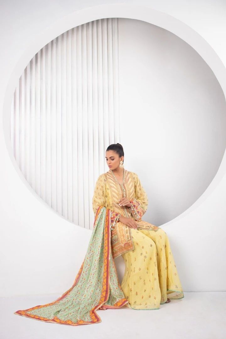 All in the details; this gorgeous festive silhouette is cut from pure cotton net in a refreshing lemon hue is detailed with gota and zardoze work with tiny tassel details on the sleeves and neckline. This short kurta and and dhaka pajama set is paired with a printed silk dupatta with gota and dhanak details. Yellow Mulmul Sharara With Traditional Drape, Yellow Semi-stitched Cotton Silk Kurta, Yellow Long-sleeved Kurta With Sheer Dupatta, Yellow Kurta With Sheer Dupatta For Festive Occasions, Yellow Straight Kurta With Sheer Dupatta, Yellow Cotton Silk Kurta With Sheer Dupatta, Yellow Long Sleeve Kurta With Sheer Dupatta, Yellow Cotton Silk Sharara For Navratri, Yellow Cotton Silk Salwar Kameez With Long Sleeves