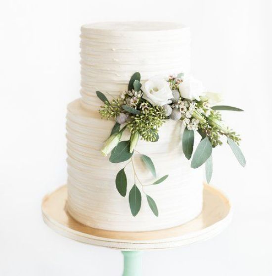 a white wedding cake with flowers and greenery on top, sitting on a wooden stand