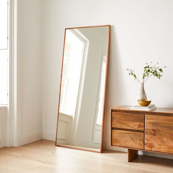 a large mirror sitting on top of a wooden dresser next to a vase filled with flowers