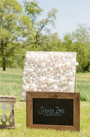 a blackboard with white balls on it next to a wooden sign that says, 28 guests throw darts at balloons filled with paint attached to a canvas you keep the art