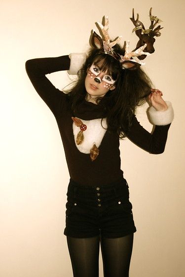 a woman with deer antlers on her head wearing black shorts and tights is posing in front of a white wall