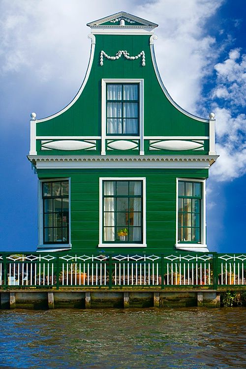 a green house sitting on top of a body of water next to a dock with a clock tower