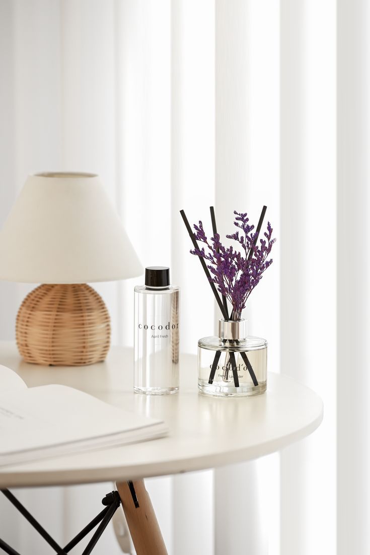 a white table topped with a vase filled with flowers next to a book and lamp