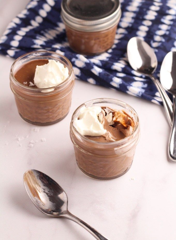 two jars filled with dessert sitting on top of a table next to silver spoons