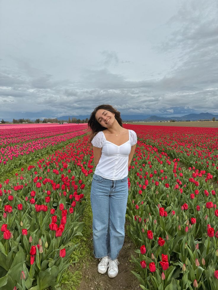 a woman standing in the middle of a field full of red tulips with her eyes closed