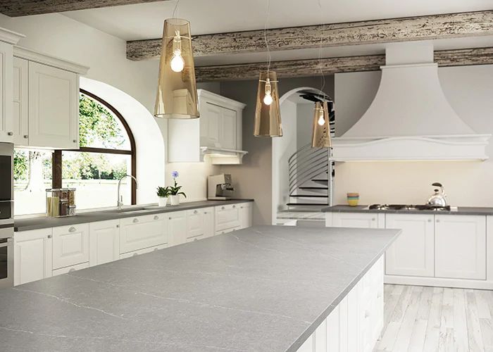 a large kitchen with white cabinets and gray counter tops, along with gold pendant lights hanging from the ceiling