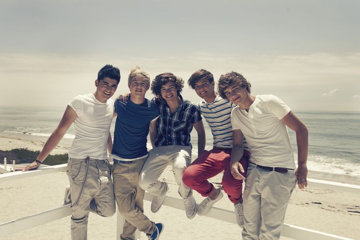 four young men posing for a photo on the beach with their arms around each other