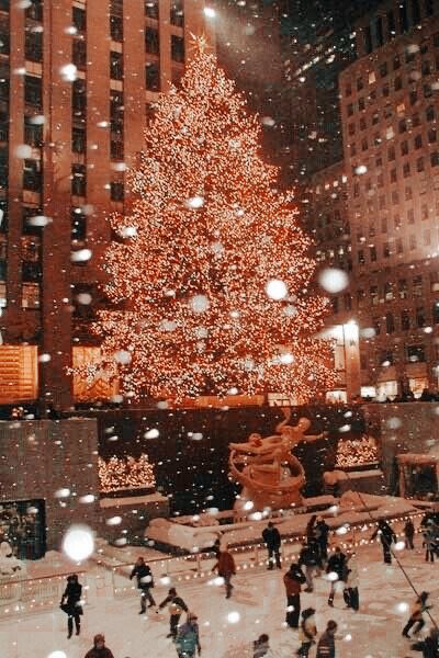 a large christmas tree in the middle of a city with snow falling all around it