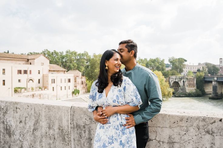 a man and woman standing next to each other on a bridge with buildings in the background