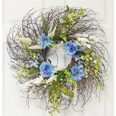 a wreath with blue flowers and greenery hanging on a white front door or wall