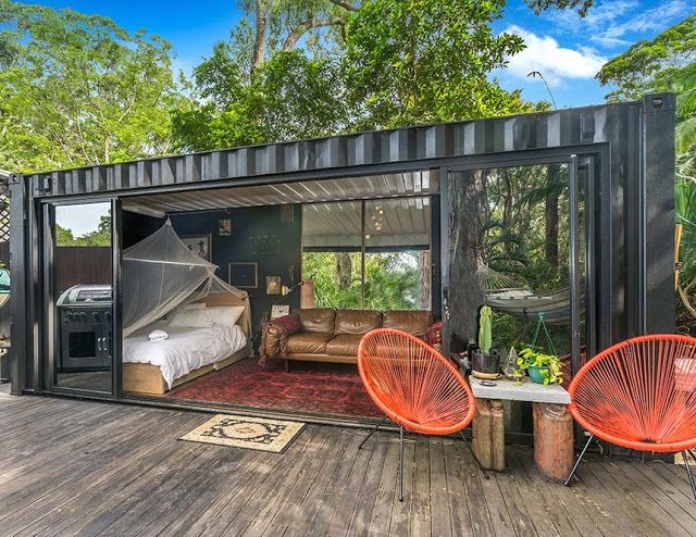 an outdoor room with two chairs and a bed in the middle of it that is made out of shipping containers