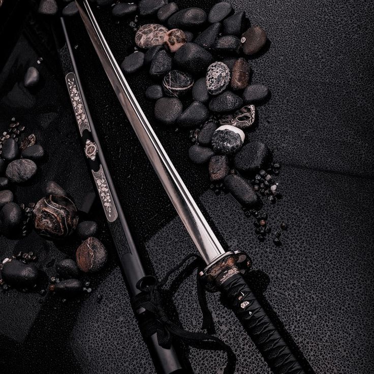 two swords are laying on the ground next to some rocks and stones, one is black with silver accents