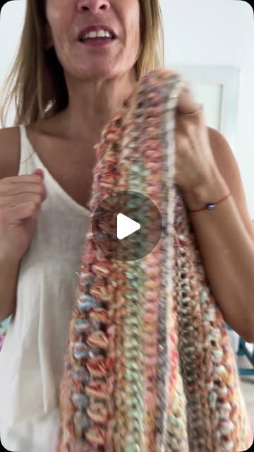 a woman is holding up a knitted scarf