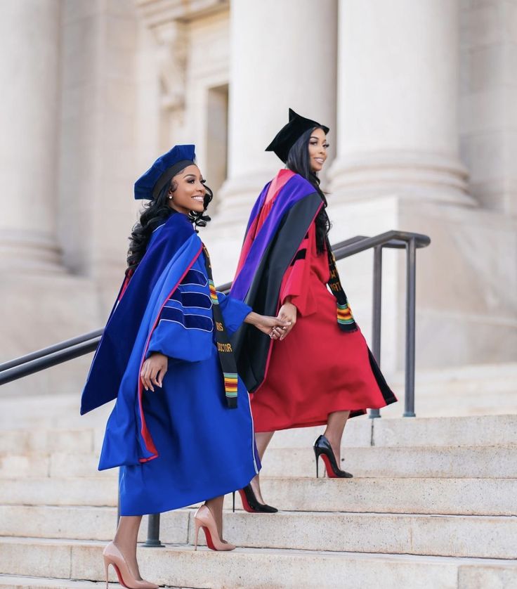 two women in graduation gowns walk down the steps together, one is holding her hand