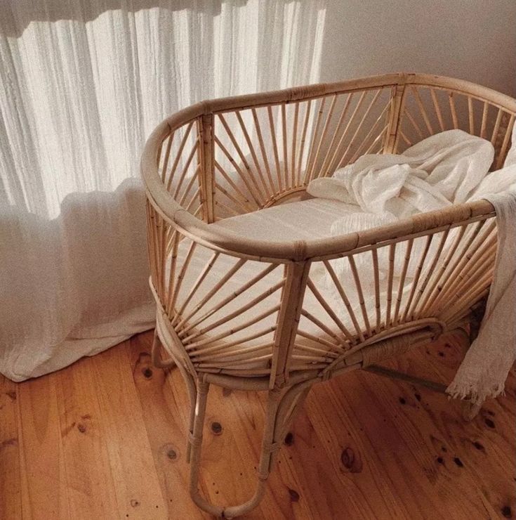 a wicker baby crib in front of a window with white drapes on it