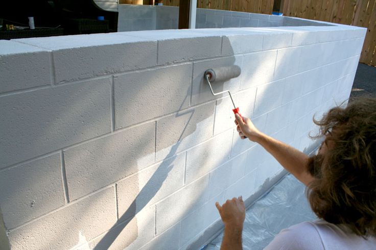 a woman is painting the side of a white brick wall with rollers on it