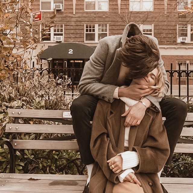 a man sitting on top of a wooden bench next to a woman in a coat