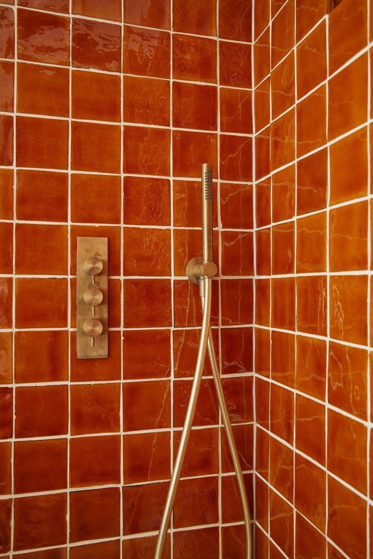 an orange tiled shower with thermostaer and hand held showerhead in it