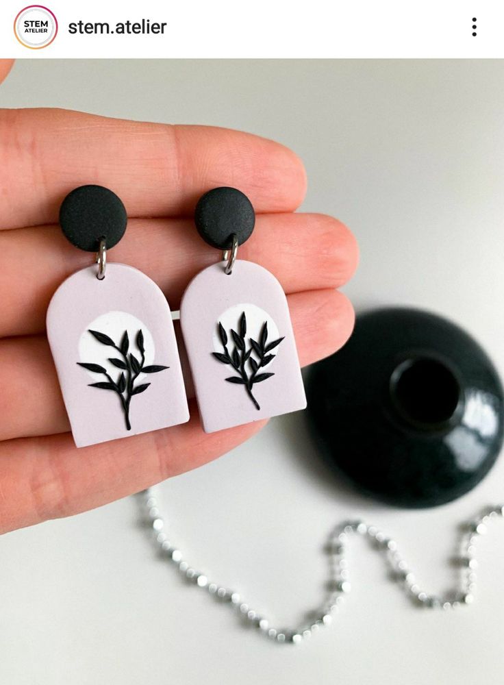 a hand holding two earrings with black and white designs on them next to a ball