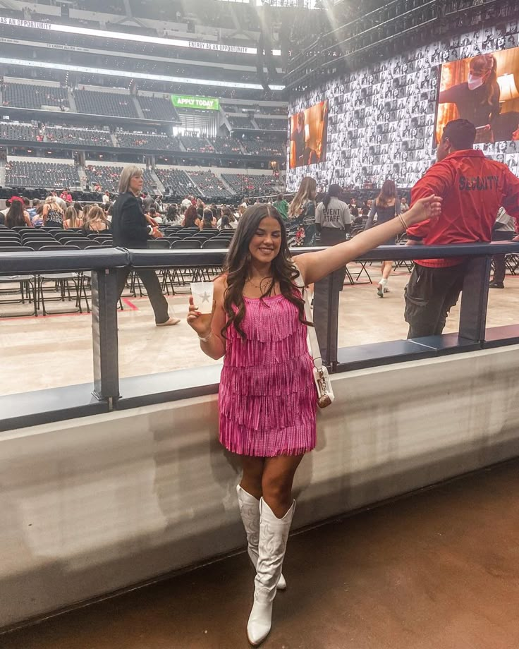 a woman in a pink dress and white boots standing next to a fence at a stadium