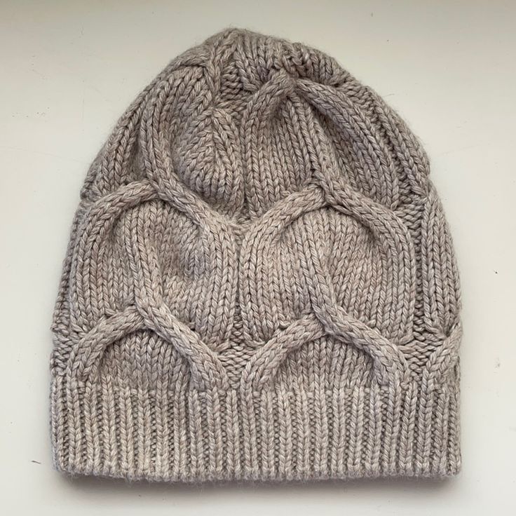 a gray knitted beanie hat on a white surface with the top knoted up