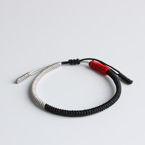 a black and white bracelet with a red bead on the end is shown against a white background