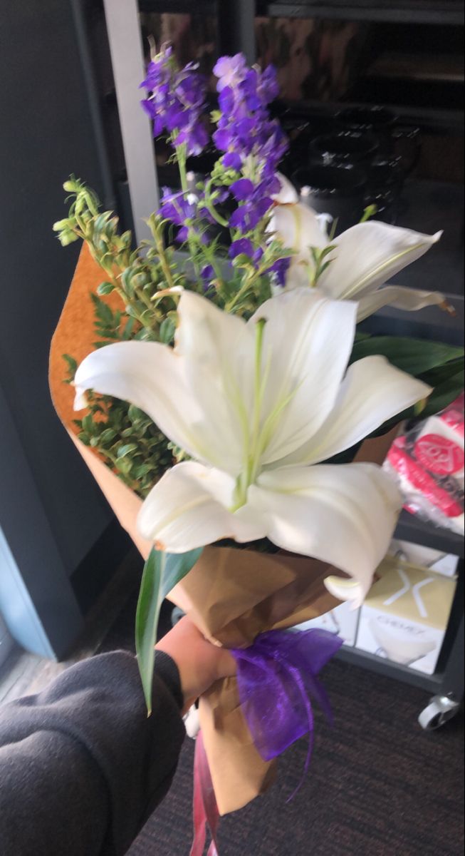 a bouquet of white lilies and purple flowers in someone's hand on the floor