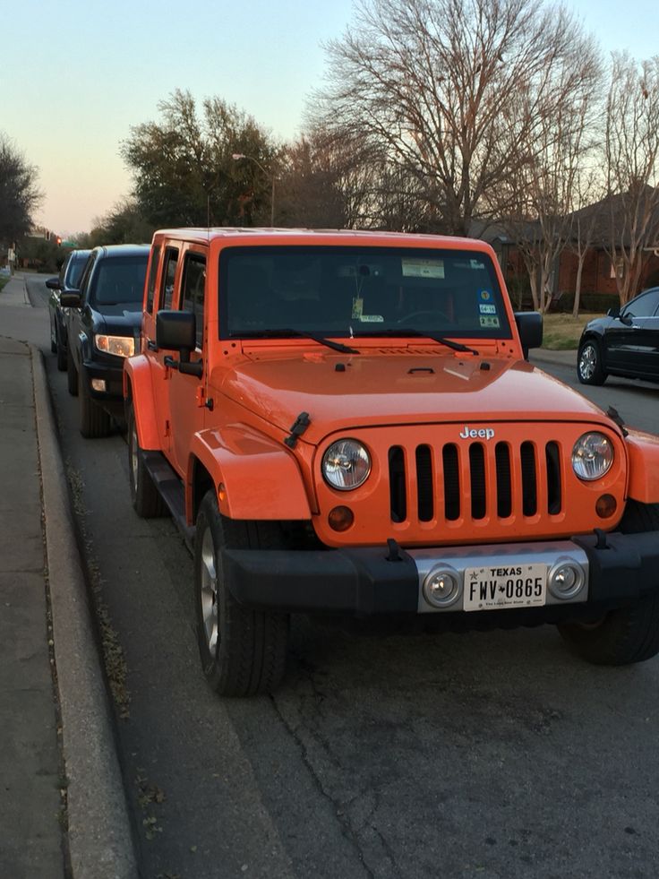 an orange jeep is parked on the side of the road in front of other cars