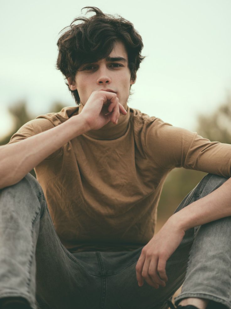 a young man sitting on the ground with his hand under his chin